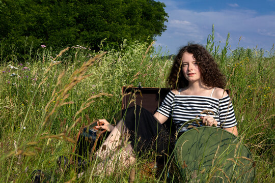 Portrait of young woman sitting in suitcase on a meadow