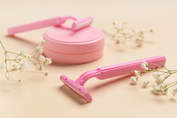 Razors for hair removal, jar of cosmetic product and flowers on color background, closeup