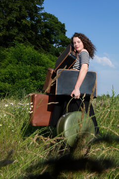 Portrait of young woman on a meadow with many suitcases