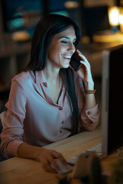 Laughing young woman on the phone working at desk in office