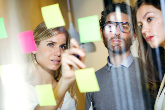 Three business people brainstorming together with sticky notes on a glass wall