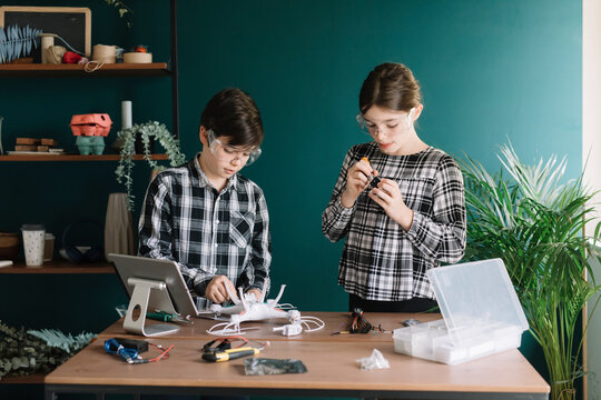 Siblings preparing drone on table while standing against wall at home