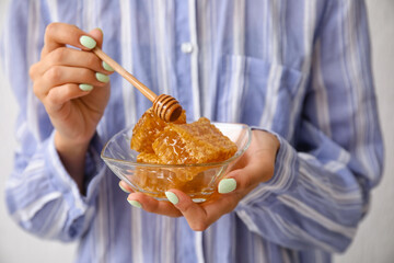 Woman holding bowl of honey combs with dipper on light background, closeup
