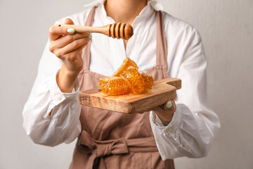 Woman pouring honey onto combs on light background, closeup