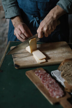 Midsection of young man cutting artisanal cheese slices on board at table
