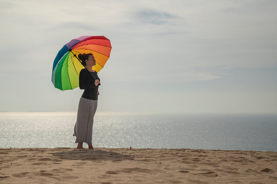 Woman with colorful umbrella standing at the beach