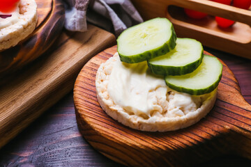Board with puffed rice crackers and cucumber on table, closeup