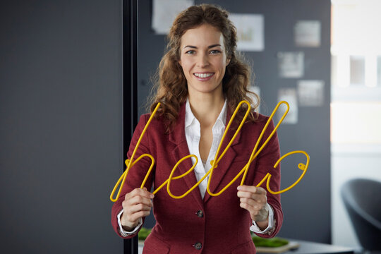 Portait of smiling businesswoman holding 'hello' neon sign in office