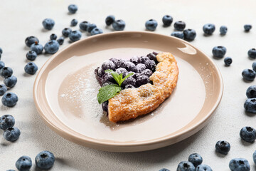 Plate with piece of tasty blueberry galette on light background, closeup