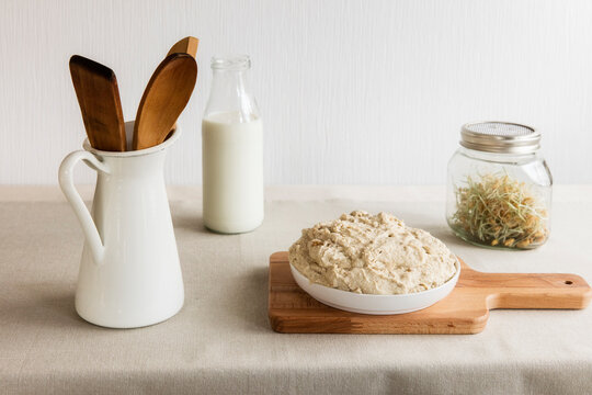 Jug with wooden spoon and spatula, milk bottle, jar of sprouts and dough on cutting board