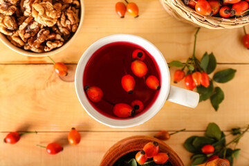 Cup of tasty rose hip tea and berries on wooden background