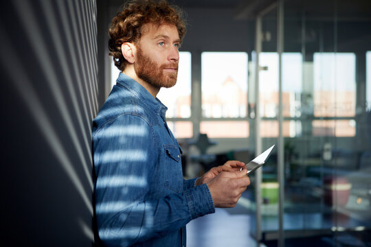 Casual businessman leaning against a wall in office using a tablet