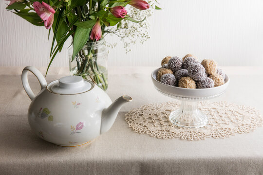 Jar with blooming flowers, bowl of protein balls and white ceramic teapot