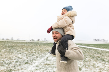 Playful father carrying daughter piggyback in winter landscape