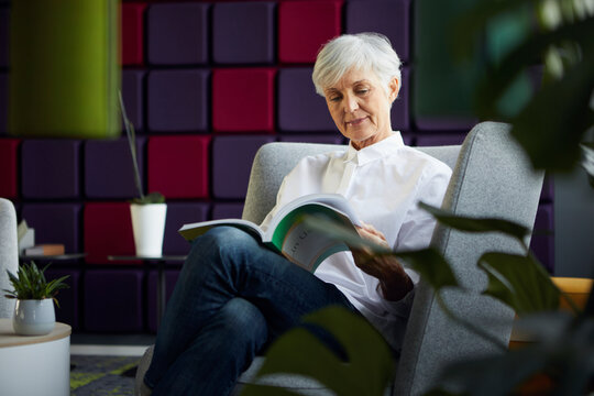 Portrait of senior businesswoman sitting on lounge chair reading