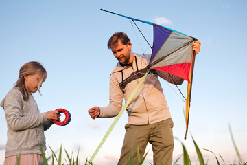 Girl holding spools while father flying kite against sky