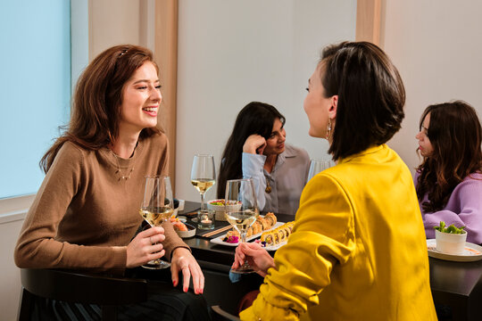 Smiling female friends with glass of white wine talking while sitting at table in restaurant