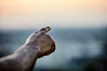 Cropped hand of man pointing at sky from building terrace during sunset