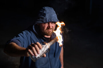 The man in the hood is holding a burning bottle. Molotov cocktail.