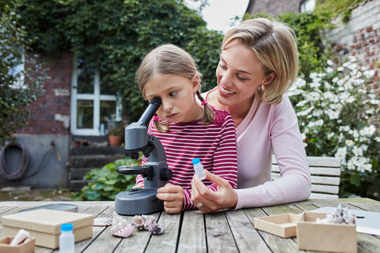 Mother and daughter using microscope together at garden table