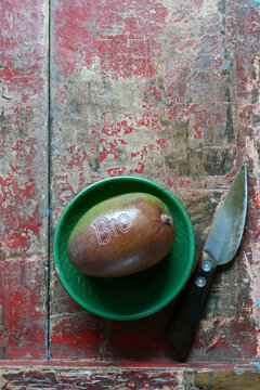 Small bowl, mango fruit and kitchen knife lying on weathered wooden surface