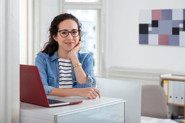 Female professional sitting by laptop at desk in office