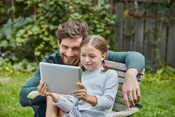Happy father and daughter using tablet together in garden