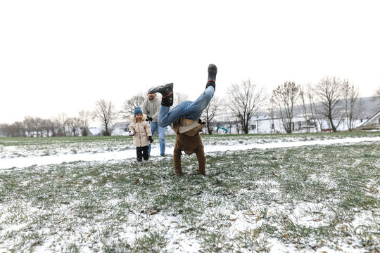 Boy doing a handstand on snowy field with family in background