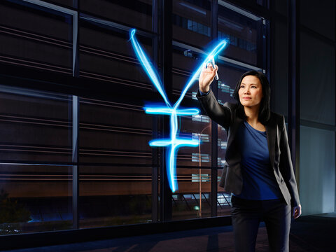 Asian businesswoman painting Yen sign with light