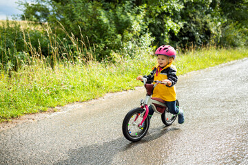 Toddler girl with pink cycling helmet on balance bicycle