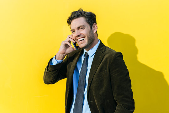 Happy businessman on the phone in front of yellow wall