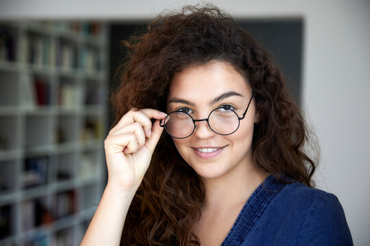 Smiling woman with long brown curly hair wearing eyeglasses at home