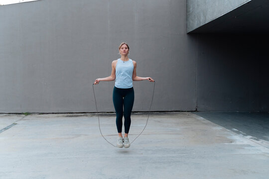 Young sportswoman skipping rope while standing against wall