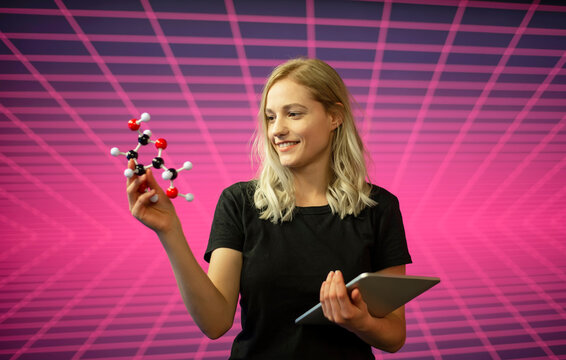 Female scientist holding molecule model and digital tablet while standing against grid pattern