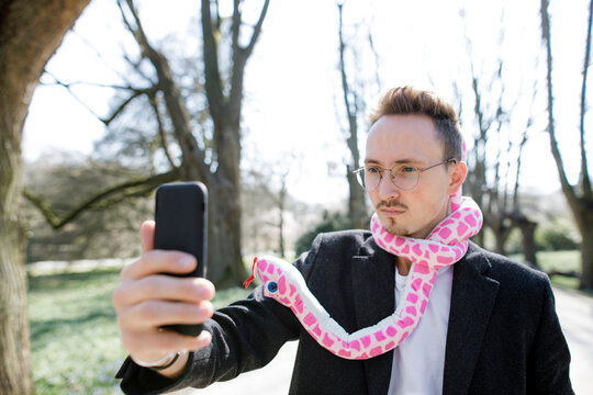 Young man wearing toy snake around his neck taking a selfie