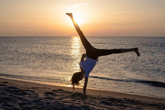 Germany, Mecklenburg-West Pomerania, Silhouette of teenage girl making handstand on beach at sunset