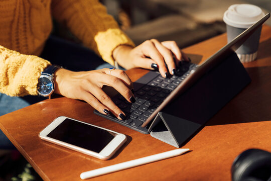 Midsection of young female student using digital tablet at sidewalk cafe table in city