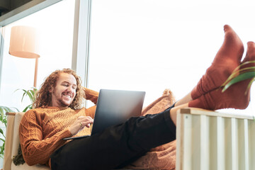 Smiling man using laptop while lying on sofa at home