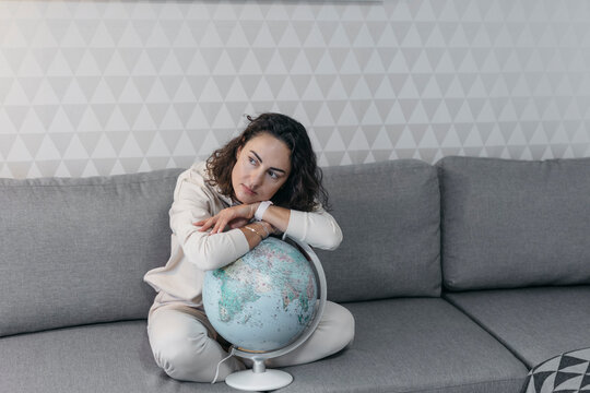 Portrait of woman sitting on the couch at home leaning on globe while looking at distance