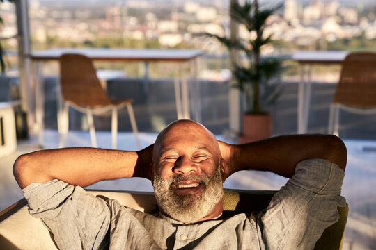 Smiling mature man relaxing on sofa at building terrace during sunset