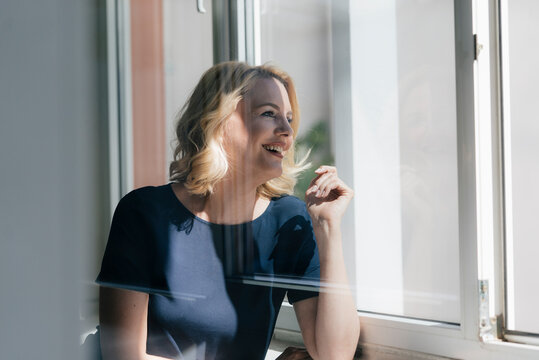 Happy blond woman in sunlight looking out of window