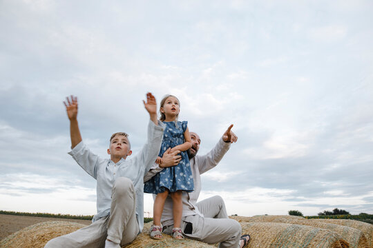 Father and his children sitting on hay bales, watching sky