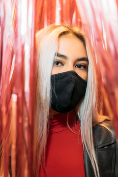 Close-up portrait of young woman wearing black mask amidst curtains