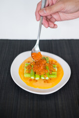 Hand puts red salmon caviar on Mini asparagus with sauce on white plate in Japanese restaurant, close up, flat lay, picture for the menu, healthy food