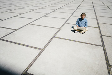 Young man sitting on a square using laptop