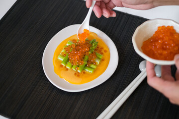 Hand puts red salmon caviar on Mini asparagus with sauce on white plate in Japanese restaurant, close up, flat lay, picture for the menu, healthy food