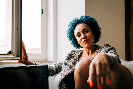 Mid adult woman with curly hair sitting by window at home