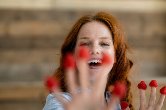 Portrait of laughing redheaded woman with raspberries on her fingertips