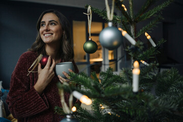 Smiling young woman decorating Christmas tree