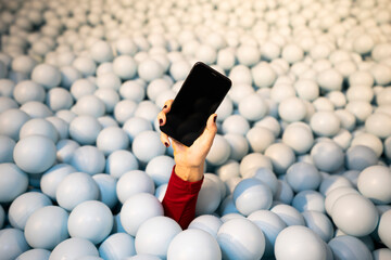 Hand of young woman holding mobile phone in ball pit
